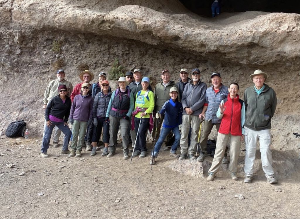 Club hikers posing for a group photo under a rock overhang on the trail
